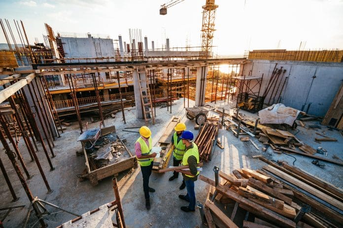 Construction industry concept - architects and engineers discussing work progress between concrete walls, scaffolds and cranes.