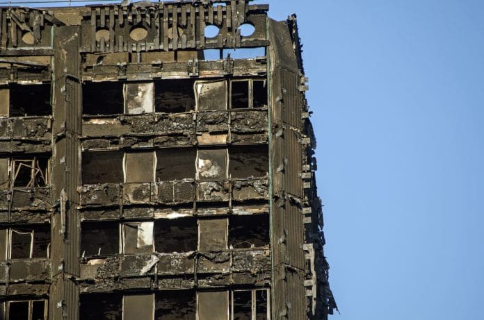 Grenfell Tower, London, a high-rise building, showing severe fire damage and broken windows against a clear blue sky after the fire of 14 June 2017.