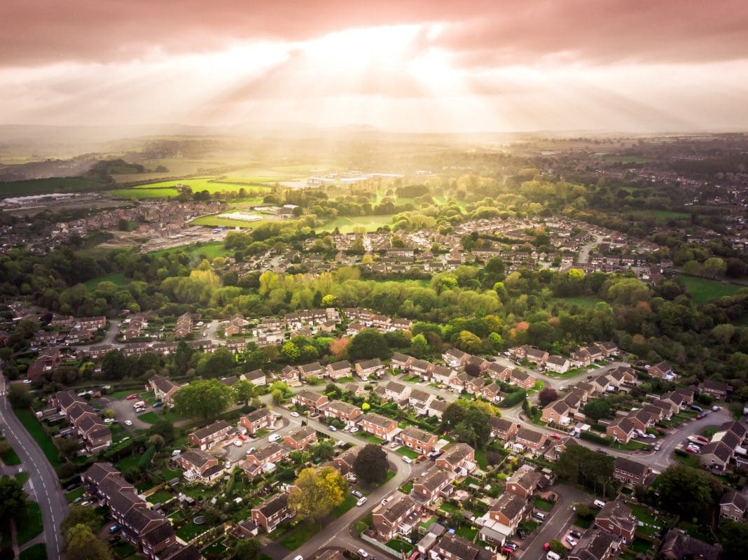 An aerial view of the sun breaking though clouds over traditional British housing illustrating the need to reimagine England's planning system