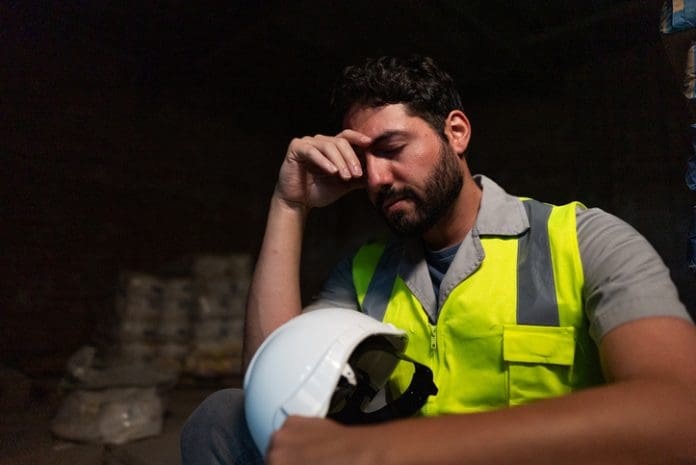 Mental health in construction: A construction worker in hi viz vest holds their head in their hand