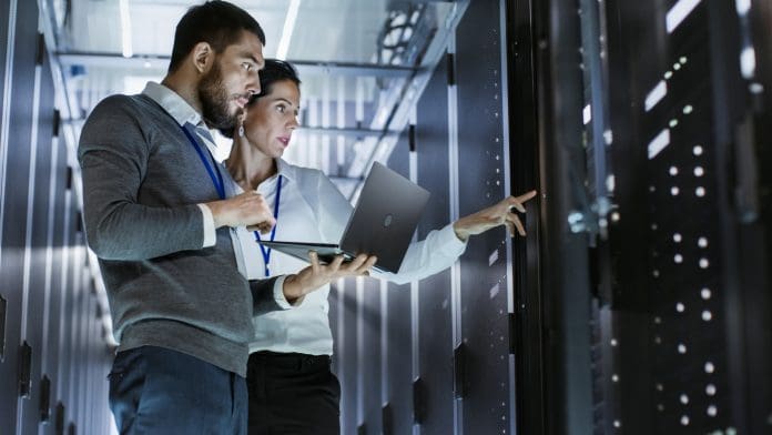 Male IT Specialist Holds Laptop and Discusses Work with Female Server Technician.