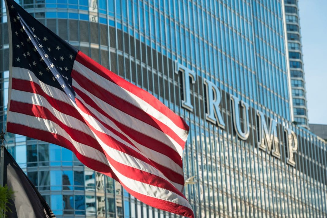 Chicago, USA - August 24, 2016: An American flag flying on the Riverwalk at the Vietnam Veterans Fountain late in the day with the Trump Tower in the background, representing potential impacts on the insurance market