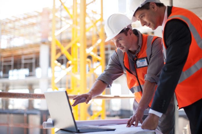 Two construction workers consult a laptop on site. Can AI progress management supercharge lean construction?