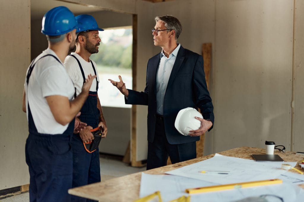 Male real estate developer talking to workers about rebuilding problems at construction site. Copy space.