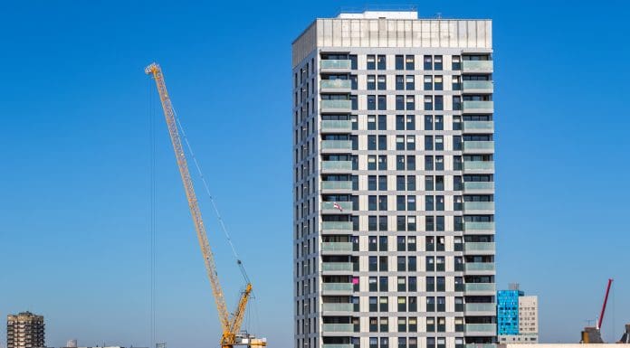 Residential new development high rise tower block with a crane in London against a cloudless sky, representing the cladding crisis