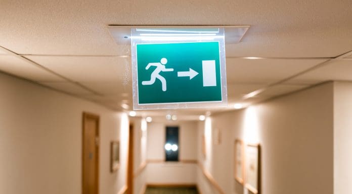 Shallow focus of a generic Fire Escape sign seen hanging from the ceiling of a hotel lobby in the UK. Seen during late at night, many of the guests are in there rooms, representing the FSBRG