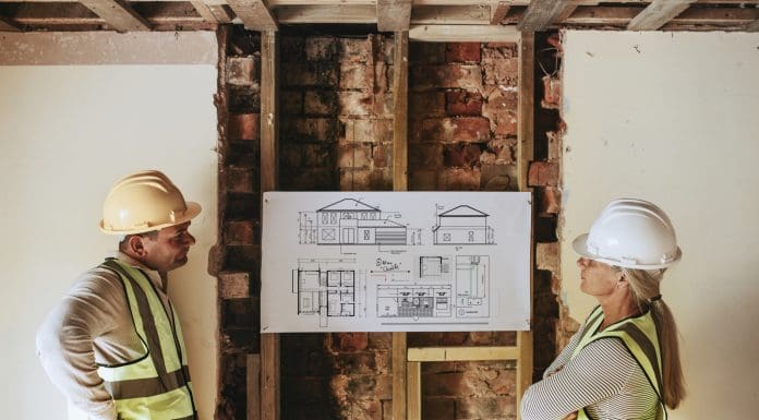 Contractor coworkers looking at floor plan at a construction site, representing UK housing demand