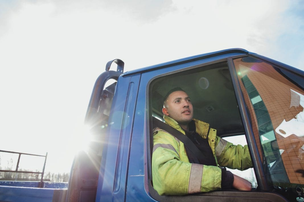 Mid-adult manual worker is pulling out of a parking lot in his pick-up truck.