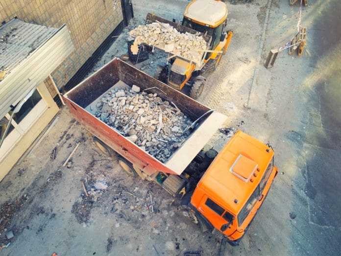 Bulldozer loader uploading waste and debris into dump truck at construction site. building dismantling and construction waste disposal service. Aerial drone industrial background