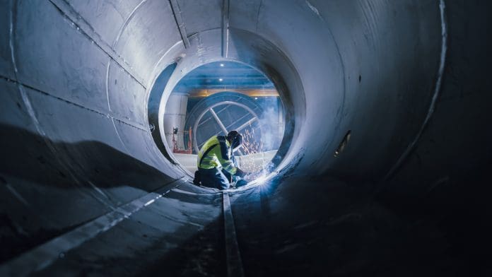 Professional Heavy Industry Welder Working Inside Pipe, Wears Helmet and Starts Welding. Construction of the Oil, Natural Gas and Fuels Transport Pipeline. Industrial Manufacturing Factory, representing subsurface mapping