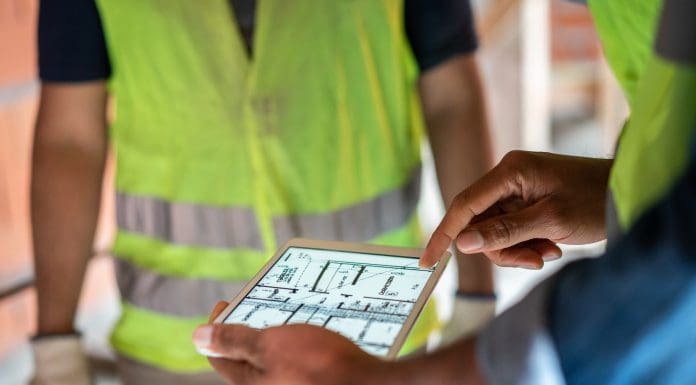 Close-up of a male architect using a digital tablet for discussing construction plan with colleagues at a construction site. Construction site engineer reviewing blueprints on digital tablet, representing building control in 2025