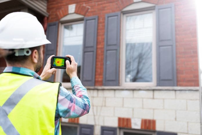 Home inspector using thermal camera to analyse the heat loss of a house