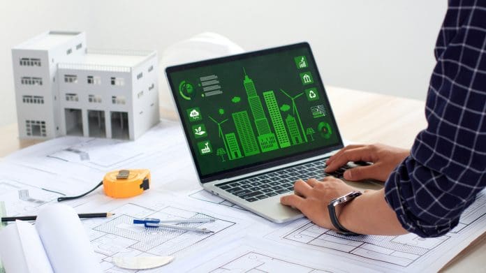 An architect uses a laptop displaying a sustainable city with blueprints and green building models. Eco-friendly building. Modern city. Green Business. Sustainable energy. Sustainable design.