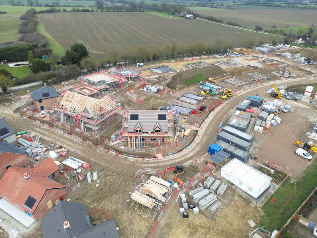 Drone view of new homes being developed in rural Essex, UK. In the distance is arable farmland. Roof beams can be seen on the detached house in the middle of the image, representing the New Towns Proposals