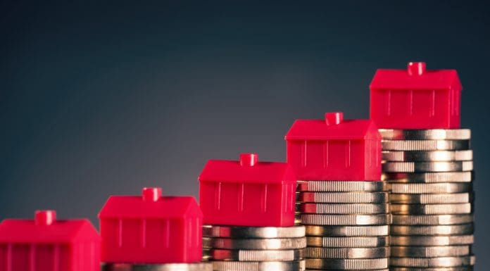 Small red houses stand on stacks of coins.