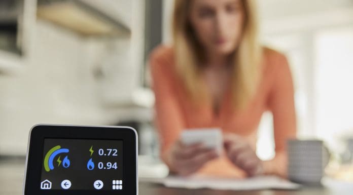 Energy Meter In Kitchen Measuring Electricity And Gas Use With Woman Looking At Bills With Calculator, representing the warm homes plan