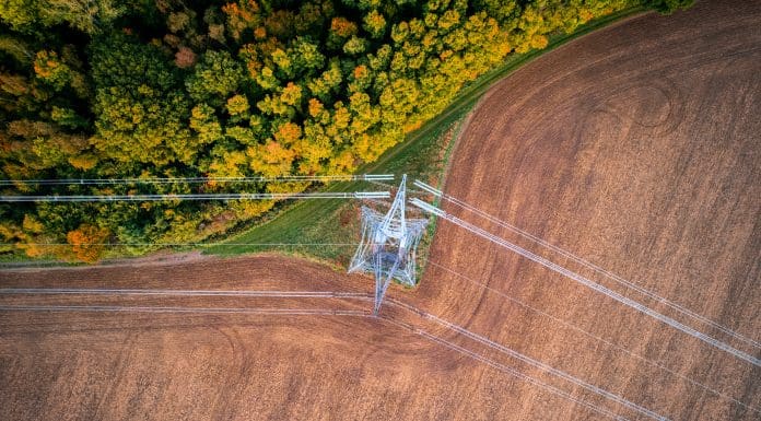 400kV extra high voltage electricity line changing direction above cultivated field contracting with autumn forest, shot from above with drone, representing the new planning and infrastructure bill