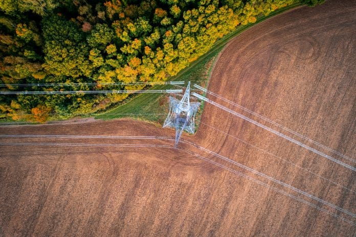 400kV extra high voltage electricity line changing direction above cultivated field contracting with autumn forest, shot from above with drone, representing the new planning and infrastructure bill