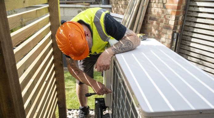 A male electrician installing a heat pump in a garden on a sunny day.