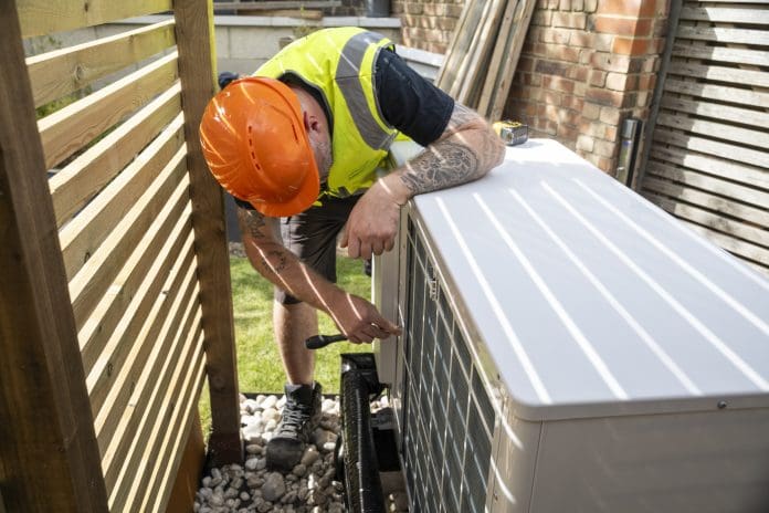 A male electrician installing a heat pump in a garden on a sunny day.